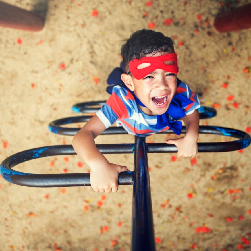 Boy in superhero costume climbing in a playground.